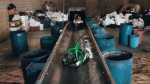 Conveyor belt em processo de reciclagem com materiais plásticos e tubos verdes sendo separados em recipientes azuis