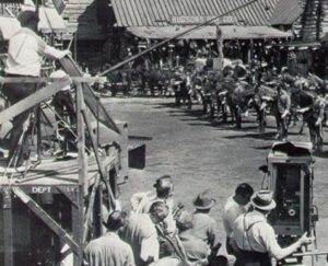 Set de filmagem dos anos 20 com equipe e atores em cena de western.